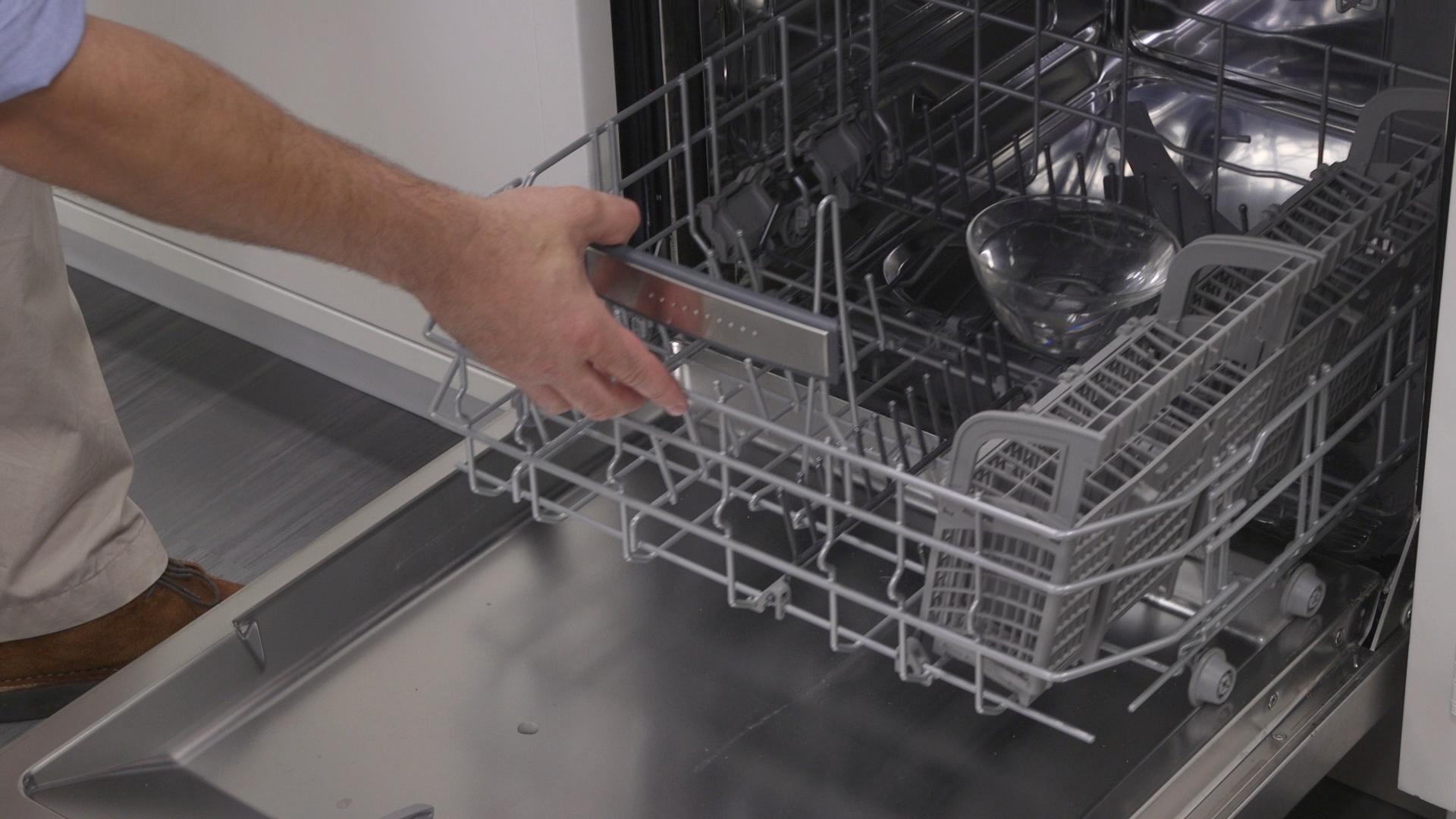 Person pulling out the bottom rack of a modern dishwasher filled with clean dishes in a home kitchen.