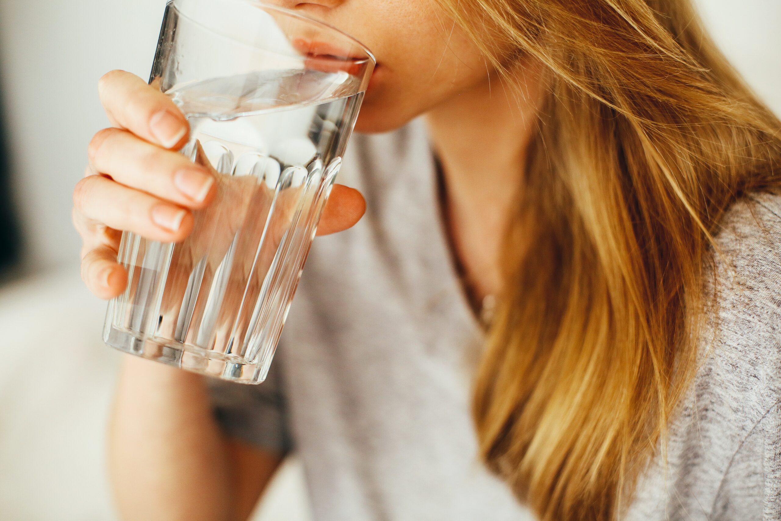 Woman drinking a glass of clean water at home, representing the importance of safe and reliable plumbing systems.
