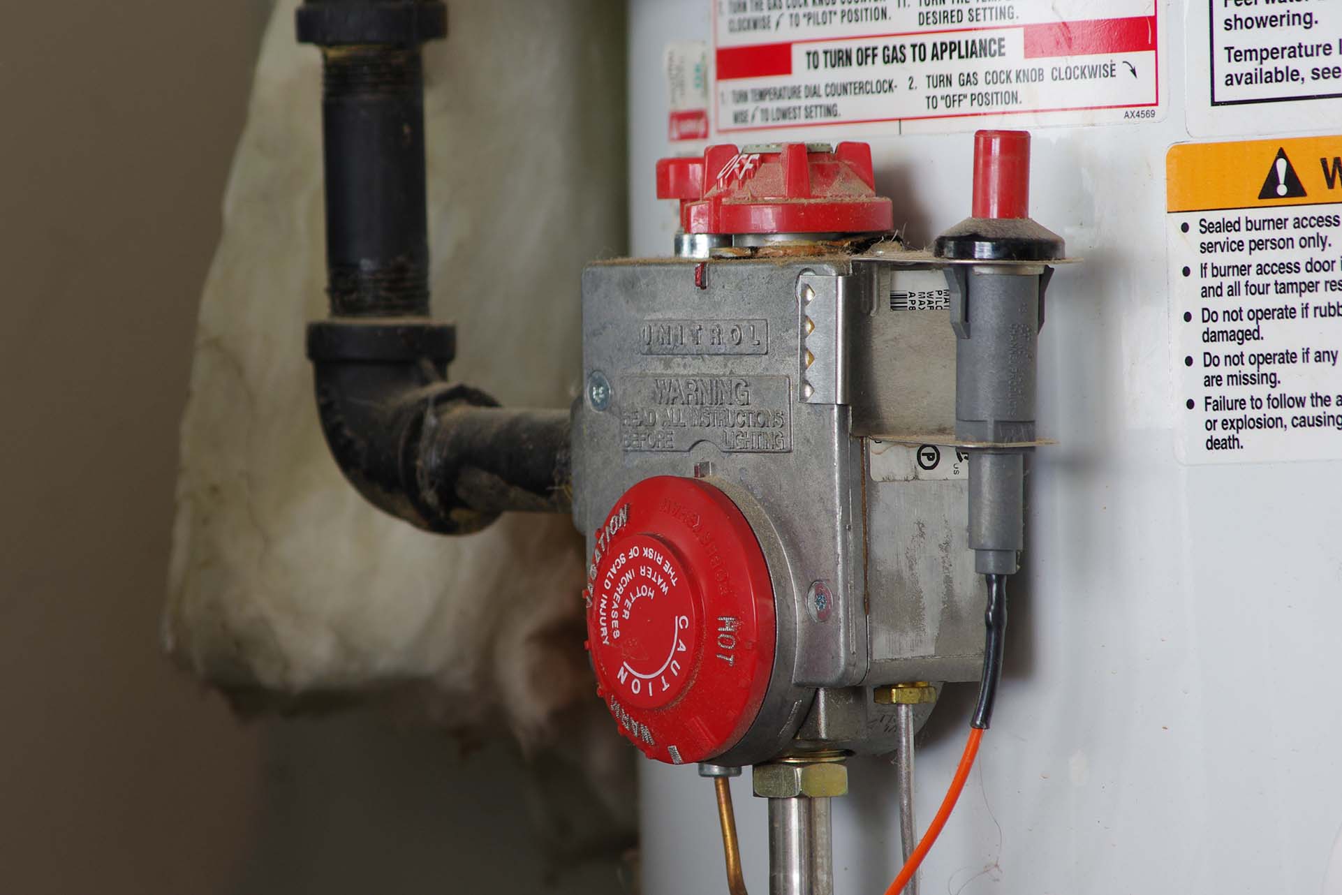 Close-up of a residential gas water heater control valve and thermostat, showing temperature settings and safety warnings.