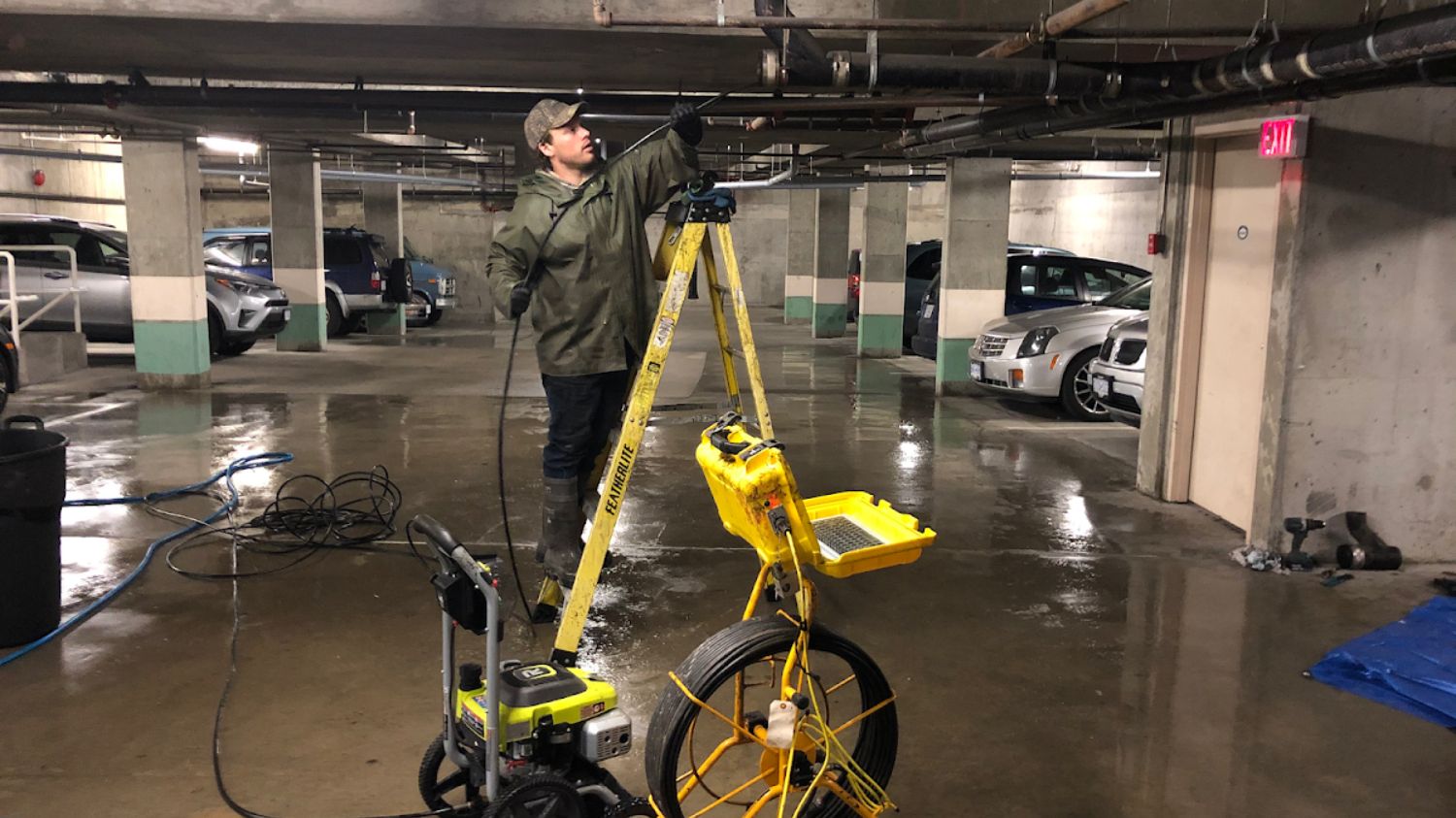 Plumber performing commercial hydro jetting in an underground parking garage, using high-pressure equipment to clear drainage lines.