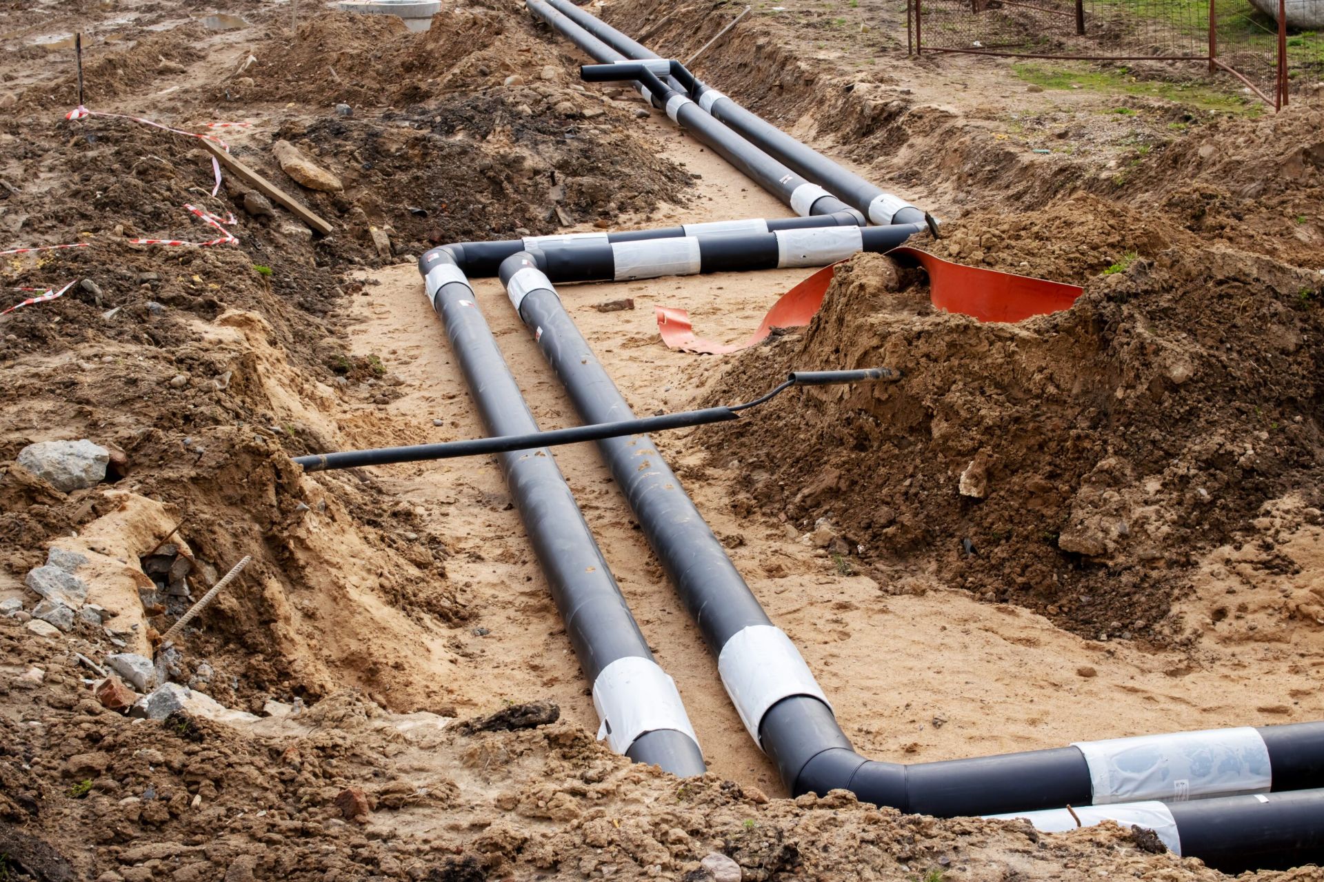 Underground drainage and sewer line installation with exposed black PVC pipes during new construction trenching work.